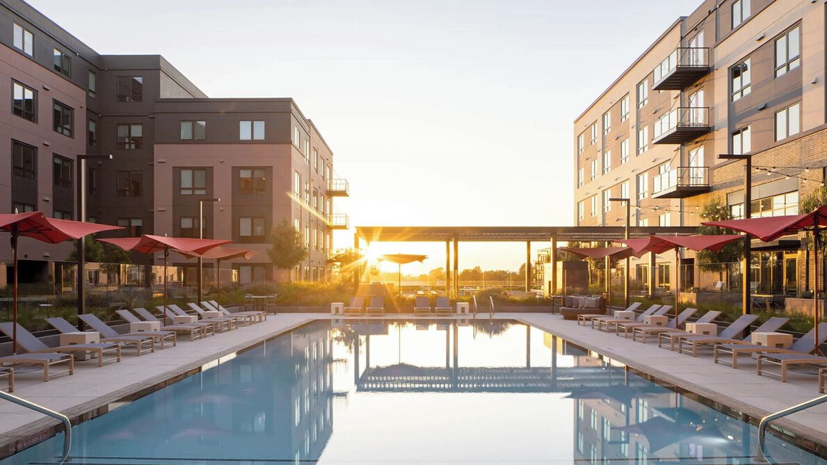 A swimming pool with lounge chairs and umbrellas, surrounded by multi-story buildings with balconies.