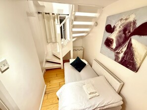 A bedroom with a bed, a painting, a staircase, and a radiator. - The Harbour Loft | En-Suite Duplex | Canada Water (London)