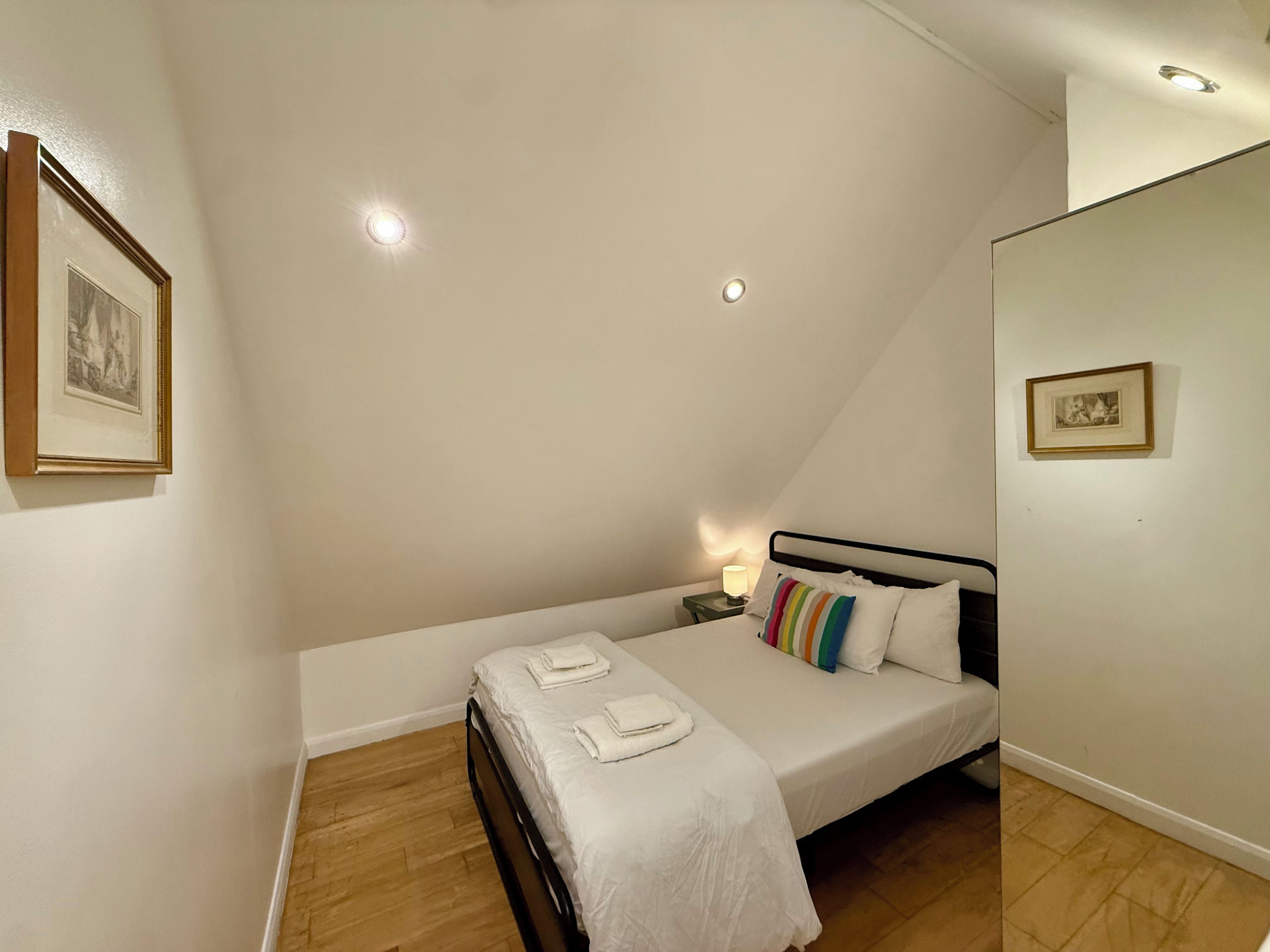 A bedroom with a bed, a nightstand, a lamp, and two framed pictures on the walls.