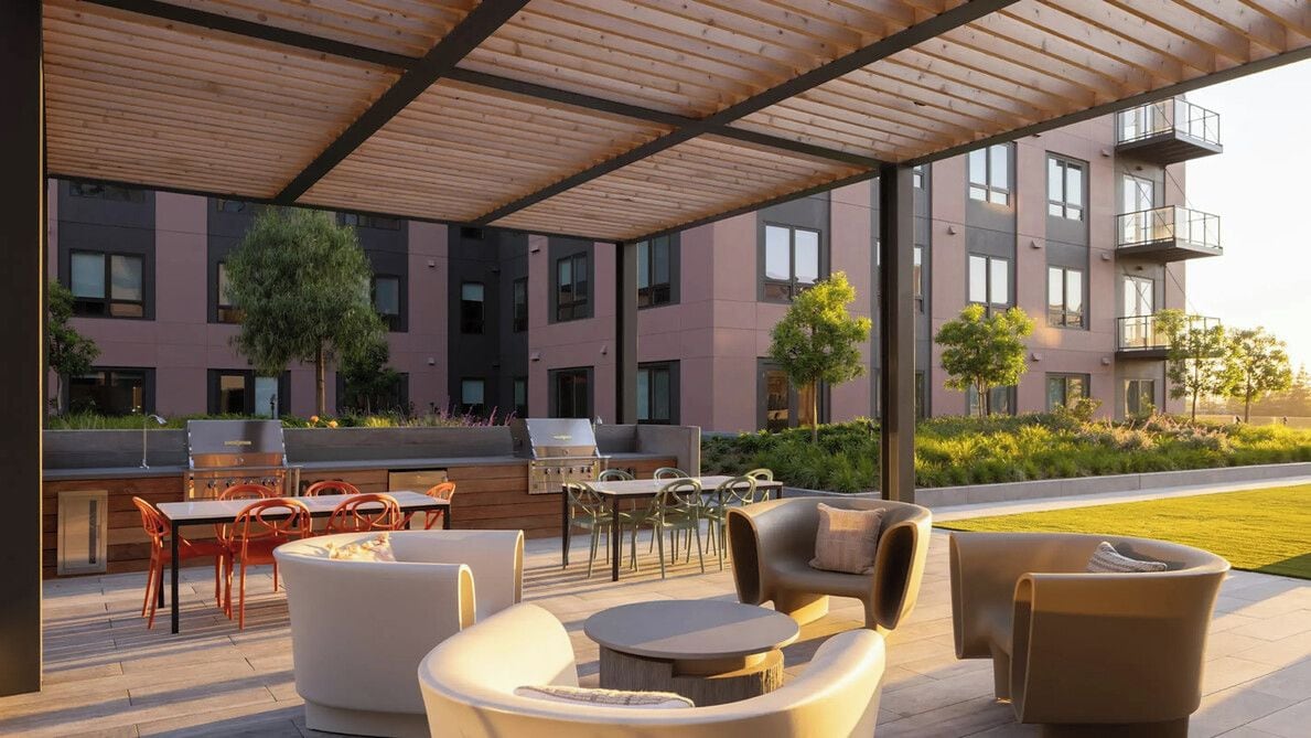 An outdoor patio with modern furniture, a barbecue grill, and a view of a multi-story building with balconies.