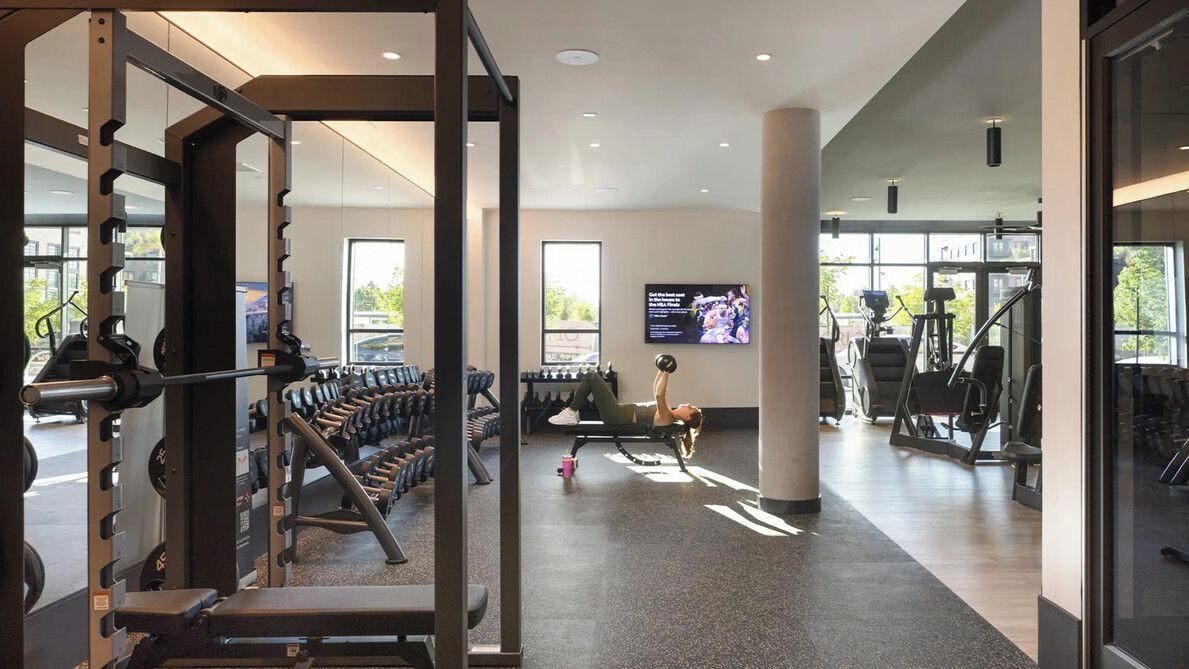 A modern gym with weightlifting equipment, cardio machines, and a TV screen.