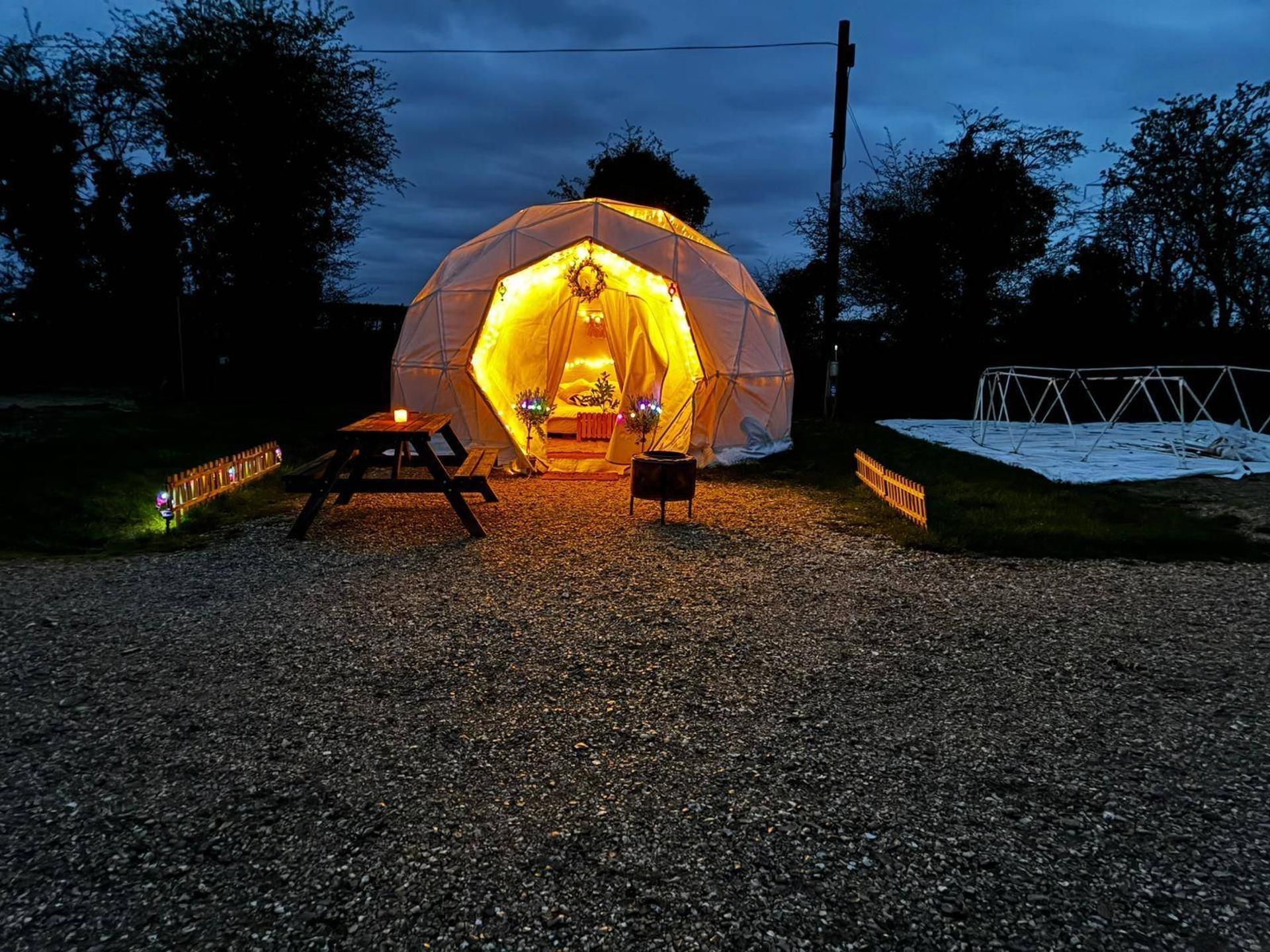 A geodesic dome structure with a central seating area, surrounded by a gravel path and a metal fence.