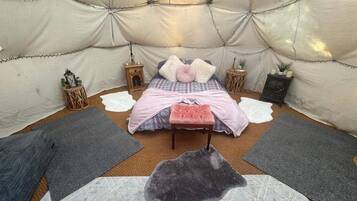A cozy interior with a bed, pillows, a rug, a small table, and a heater.