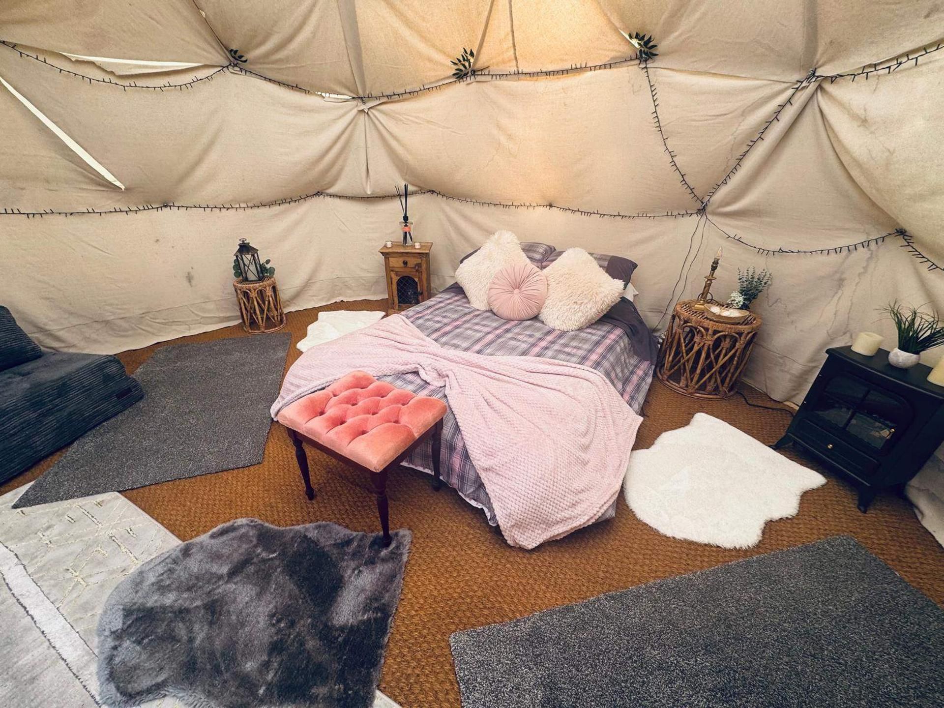 A cozy tented room with a bed, a bench, and various rugs.