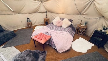 Um quarto coberto por uma tenda, com uma cama, um banco e vários tapetes.