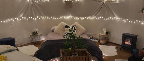Una habitación acogedora con cama, una pequeña mesa de madera con una planta, un aplique de pared y una chimenea.