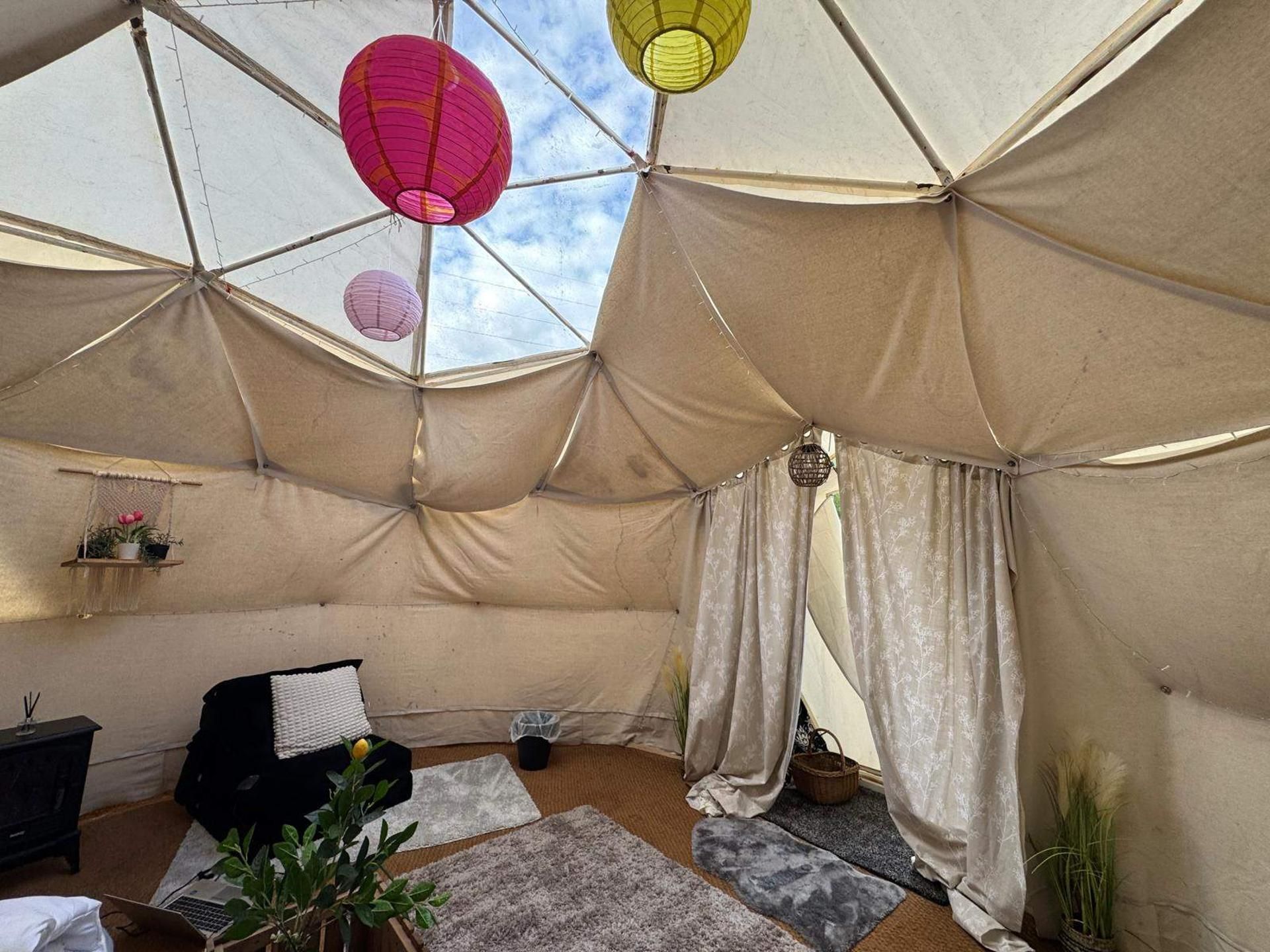 Een tentaccomodatie met uitzicht op de lucht, een zwart bankje, een klein tafeltje en een potplant.