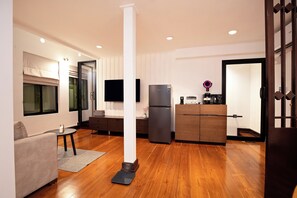 A modern living room with a sofa, a coffee table, a flat-screen TV, a refrigerator, and a wooden cabinet. - VISTA HOUSE (Bangkok)