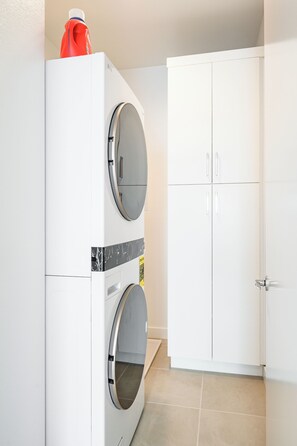 A laundry room with a front-loading washer and dryer, a white cabinet, and a tiled floor. - Modern Desert Retreat 3BR Home w/ Community Pool (Palm Desert)