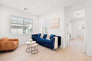 A modern living room with a blue sofa, a brown armchair, and a small round table with a vase of flowers. - Modern Desert Retreat 3BR Home w/ Community Pool (Palm Desert)