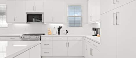 A modern kitchen with white cabinetry, a built-in oven, and a coffee machine.
