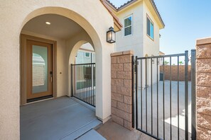 A building entrance with a door, an arched doorway, a small balcony, and a gated driveway. - Modern Desert Retreat 3BR Home w/ Community Pool (Palm Desert)