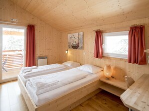 A wooden cabin room with two beds, a window with curtains, a wall-mounted lamp, and a painting. - Cabin in Turrach With Sauna and Wi-fi (Stadl-Predlitz)
