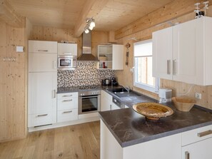 A modern kitchen with wooden walls, white cabinets, a tiled backsplash, and a marble countertop. - Cabin in Turrach With Sauna and Wi-fi (Stadl-Predlitz)