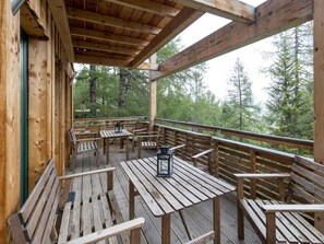 Eine Holzterrasse mit Tischen und Bänken mit Blick auf eine bewaldete Landschaft.