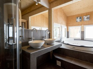 Ein modernes Badezimmer mit Duschkabine aus Glas, zwei Waschbecken mit Aufsatzwaschbecken, einer freistehenden Badewanne und Holzvertäfelung an den Wänden.