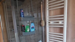 Un angolo doccia con porta in vetro, un portasciuga asciugamani bianco e uno scaffale con articoli da toilette.