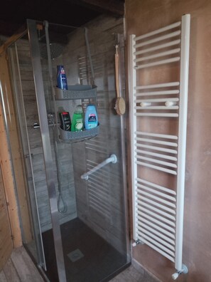 A shower area with a glass door, a white towel rack, and a shelf with toiletries. - Vrbo Property (Muffo)