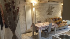 Zona pranzo con tavolo imbandito per quattro persone, divano con una coperta decorativa e un elemento decorativo a parete.