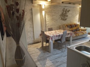 A dining area with a table set for four, a sofa with a patterned throw, and a decorative wall piece. - Vrbo Property (Muffo)