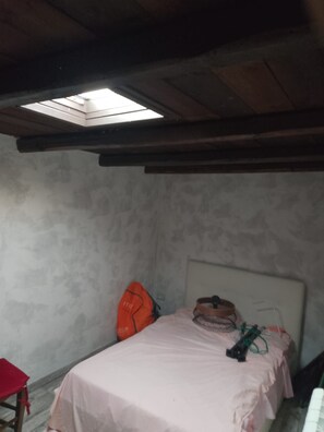 A small, dimly lit room with a single bed, a red chair, and a slanted ceiling with a skylight. - Vrbo Property (Muffo)