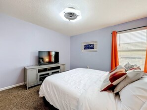 A hotel room with a bed, a television on a cabinet, and a window with curtains. - Jax Beach Haven 4 bd/Movie Room/Dinning/ Downtown (Jacksonville)