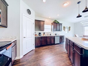 A modern kitchen with dark wood cabinets, a white door, and a large island with a countertop. - Jax Beach Haven 4 bd/Movie Room/Dinning/ Downtown (Jacksonville)