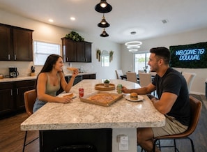 A modern kitchen with dark cabinets, a marble countertop, and a neon sign. - Jax Beach Haven 4 bd/Movie Room/Dinning/ Downtown (Jacksonville)