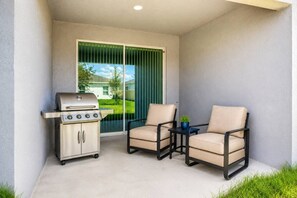 A balcony with a grill, two chairs, and a small table with a plant. - Extended Stay Winter haven, Eagle Lake, & Lakeland (Eagle Lake)