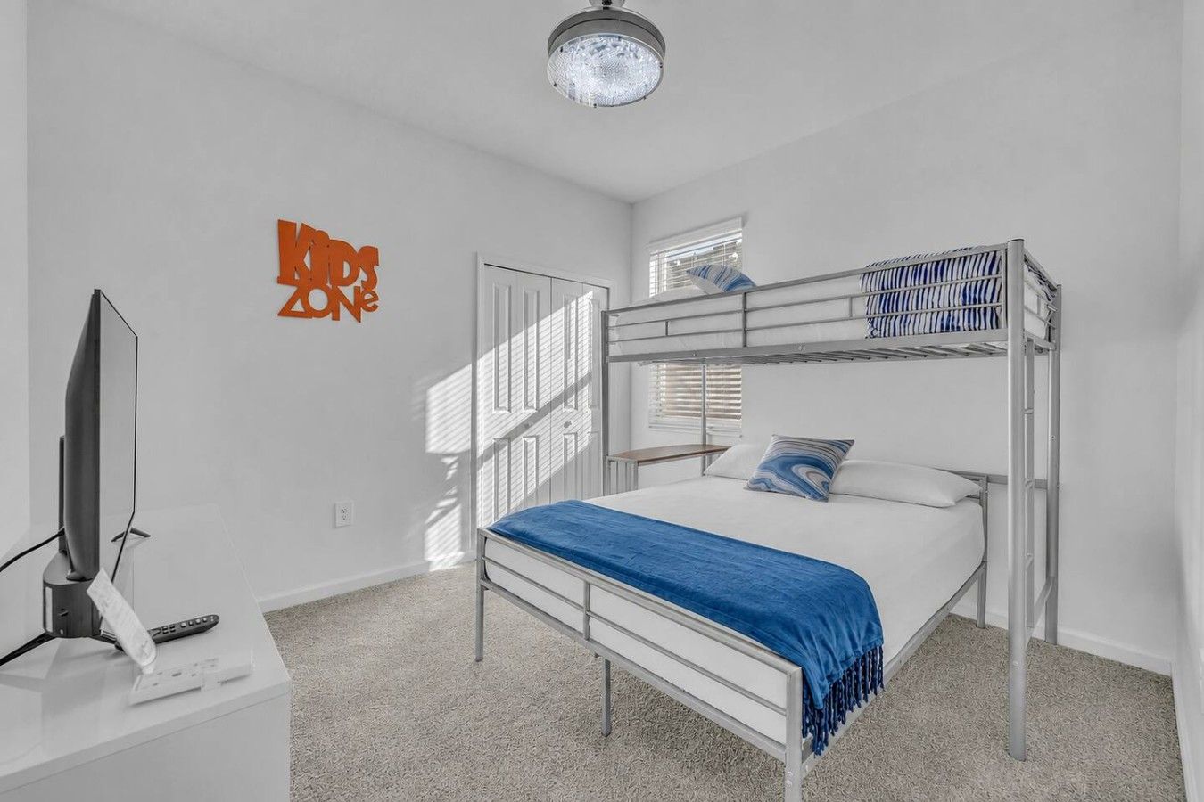 A bunk bed room with a television on a stand, a wall-mounted sign, and a window with blinds.