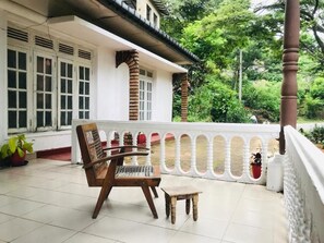 Varanda com cadeira e mesa de madeira, corrimão branco e plantas em vasos.