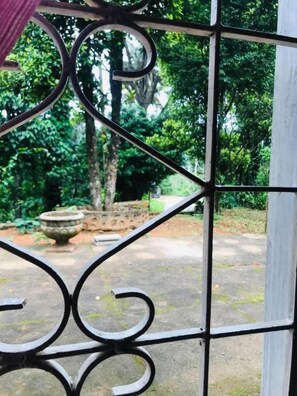 Um portão de metal com um design decorativo, dando acesso a uma área externa com vegetação e uma estrutura de pedra.