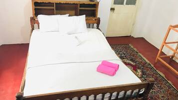 A bed with a wooden frame, white bedding, and a pink towel.