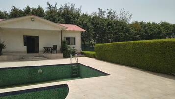 A house with a swimming pool, a covered patio, and a well-maintained hedge.