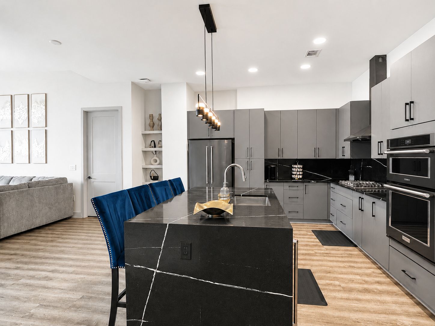 Une cuisine moderne avec des meubles gris, un îlot central noir, des appareils électroménagers en acier inoxydable et une chaise bleue.