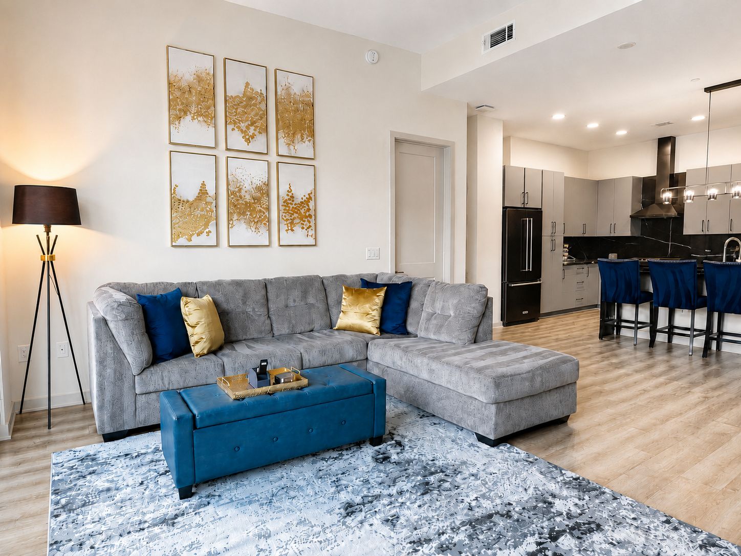 Una sala moderna con un sofá seccional gris, un otoman azul y una alfombra estampada.