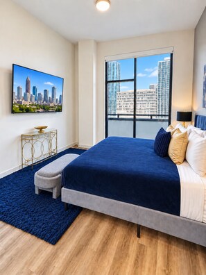 A bedroom with a large bed, a cityscape view, a television, and a small table. - Downtown Penthouse | 2 King BD/ 2 BA| Year-round Pool | Balcony |Walk Everywhere (Atlanta)