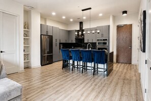 A modern kitchen with grey cabinets, a stainless steel refrigerator, an oven, and a built-in island with blue bar stools. - Downtown Penthouse | 2 King BD/ 2 BA| Year-round Pool | Balcony |Walk Everywhere (Atlanta)