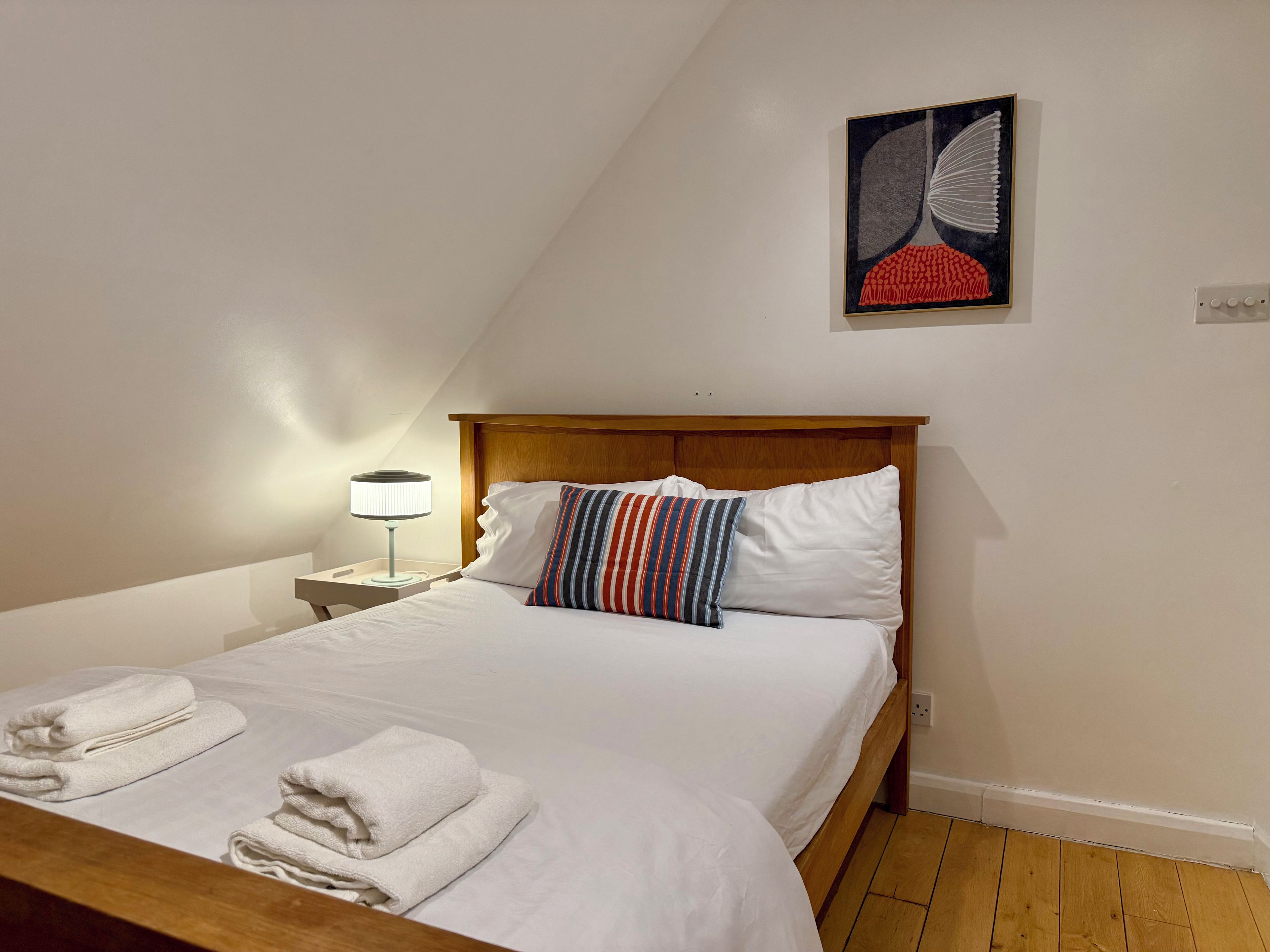 Una cama individual con ropa de cama blanca, un cojín a rayas y una lámpara de noche.