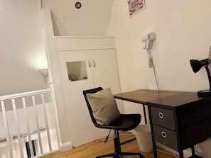 Una habitación con escritorio, silla, armario y un pequeño cubo de basura.