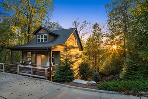 A cabin with a porch, surrounded by trees and a sunset. - Spacious w/ Game Room + Hot Tub | Mins to Downtown (Woodfin)