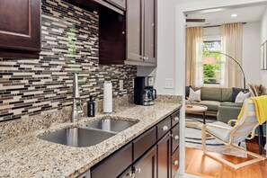 A modern kitchen with a granite countertop, stainless steel sink, and a coffee maker. - Spacious w/ Game Room + Hot Tub | Mins to Downtown (Woodfin)
