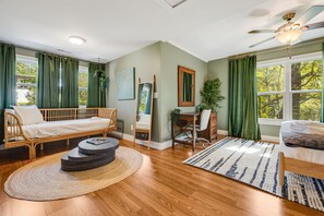 Ein Zimmer mit einem Bett, Schreibtisch und Stuhl, einem runden Couchtisch und einem großen Fenster mit Vorhängen.