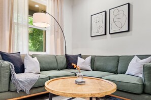 Ein Wohnzimmer mit einem grünen Sofa, einem runden Couchtisch und zwei abstrakten Kunstwerken an der Wand.