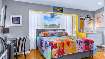 A bedroom with a bed, a desk, a chair, a window with curtains, and artwork on the walls.