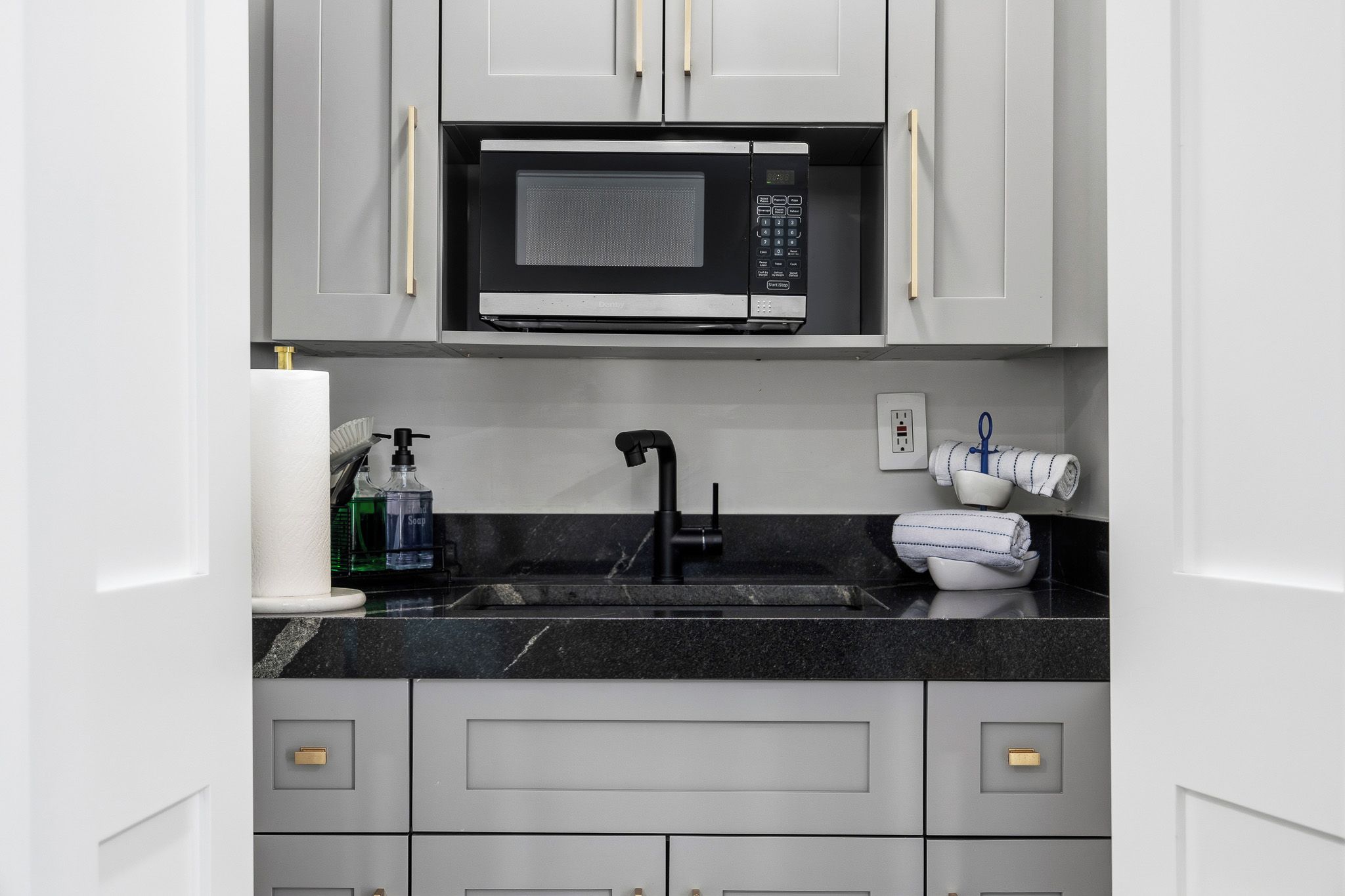 A modern kitchen with a built-in microwave, a sink with a faucet, and a countertop with various items.