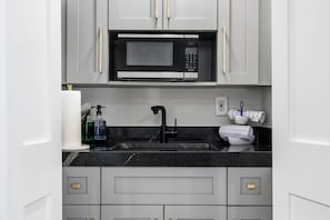Een moderne keuken met een inbouwmagnetron, een spoelbak met kraan en een aanrecht met diverse spullen.