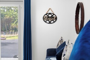 A room with a window, a wall-mounted sign that reads 'Blessed,' a curtain, and a bed with pillows. - Cozy Renovated Studio on Palm Tree & Alpaca / Llama Farm (Palm Beach Gardens)