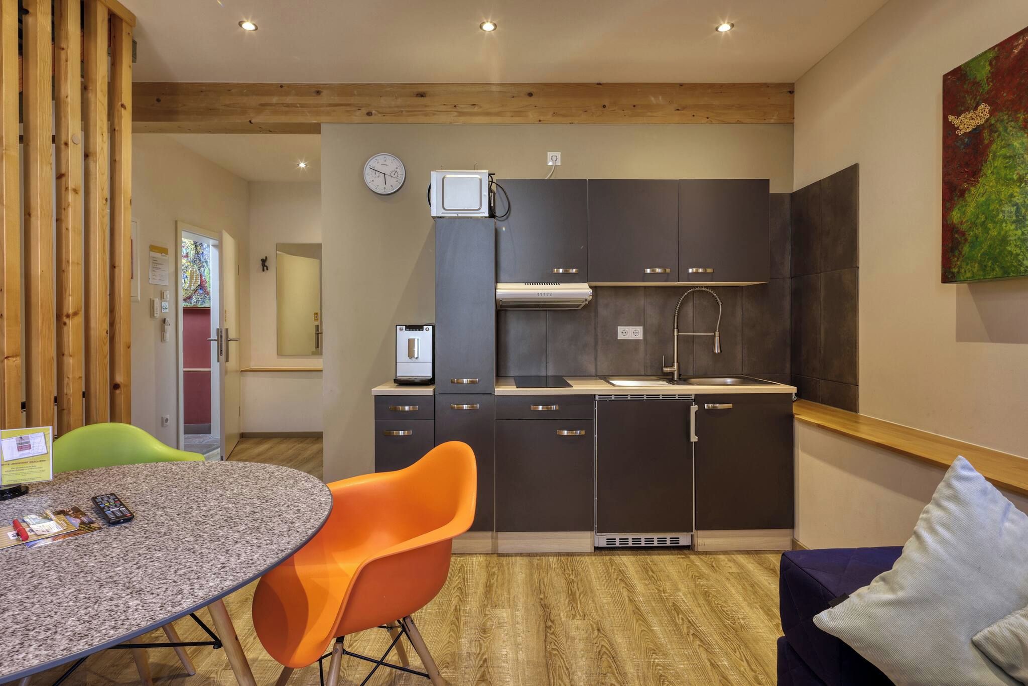 A modern kitchen with dark cabinets, a built-in oven, and a microwave. There is a dining table with a chair and a small rug.