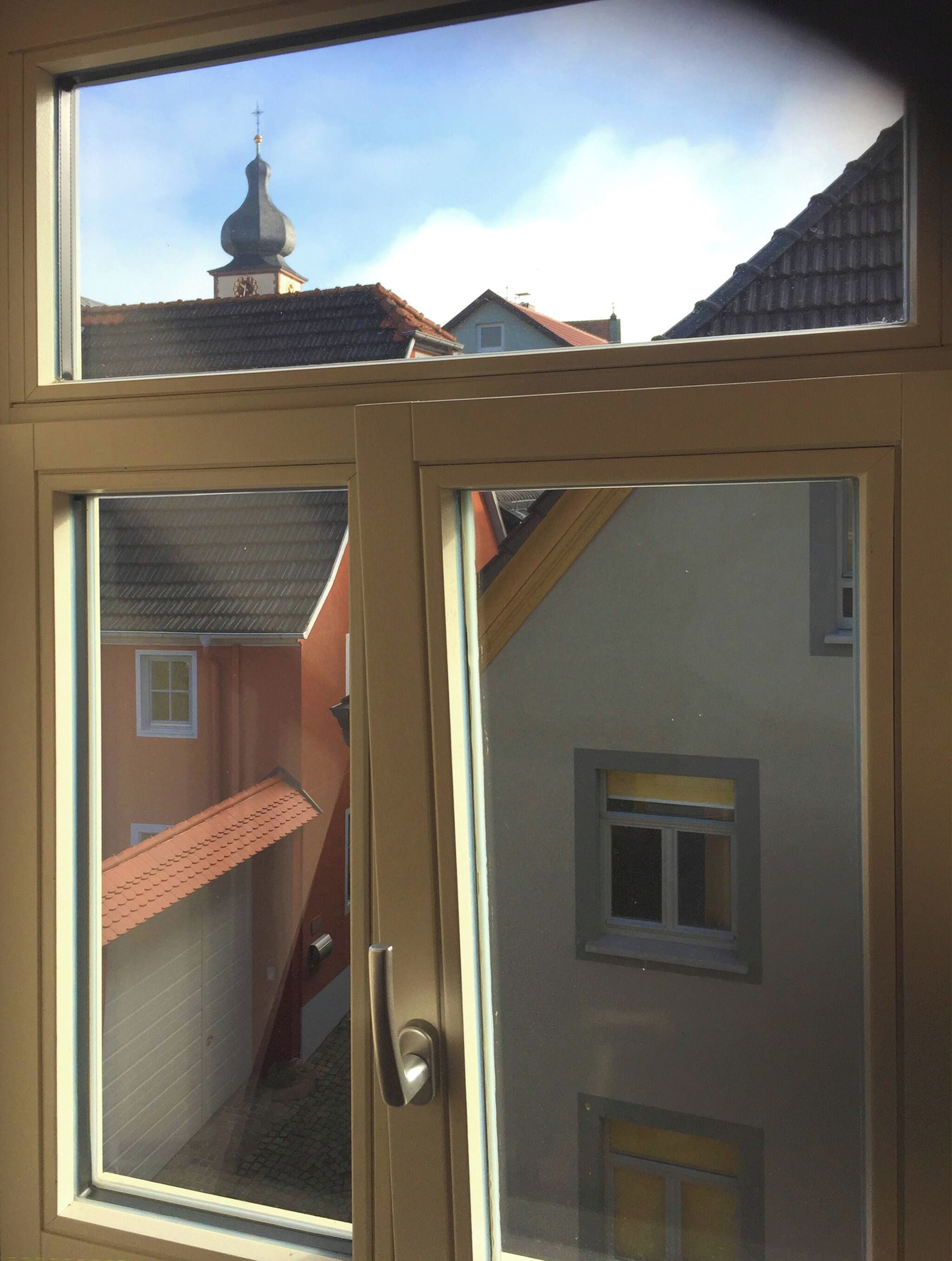 A window with a view of a building with a red roof and a tower with a cross on top.